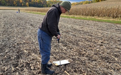 person standing in a harvested field using a penetrometer to test for soil compaction