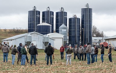 group of farmers standing in a field with blue harvestors in the background, early spring